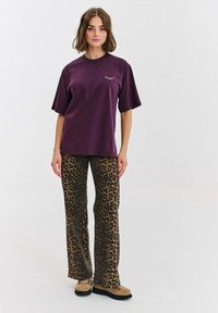 Fialové bavlněné tričko s krátkým rukávem a malou grafikou. V páru s hnědými kalhotami s leopardím potiskem a béžovými šněrovacími botami.