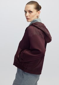 Chaqueta con capucha de color marrón con un frente texturizado y mangas lisas. Los puños y el dobladillo acanalados ofrecen un ajuste ceñido y cuenta con bolsillos laterales.