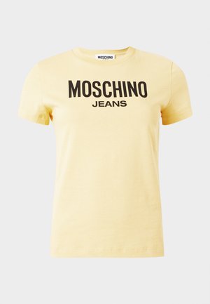 Světle žluté tričko s krátkým rukávem a černým logem "MOSCHINO JEANS" uprostřed na přední straně proti jednoduchému pozadí.