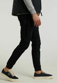 Pantalones ajustados negros con bolsillos laterales y detalles texturizados, combinados con zapatillas de lona azul marino con cordones crema y suela clara.