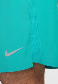 Calções atléticos turquesa feitos de tecido respirável, com um painel em rede e um logótipo prateado da Nike na parte inferior esquerda.