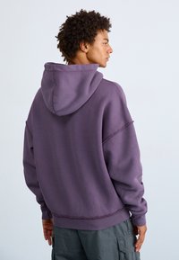 Übergroßer lila Hoodie mit Kapuze und Kordelzug, strukturierter Stoff und gerippten Bündchen. Hat einen lockeren Schnitt und sichtbare Nähte.