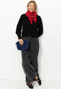 Cardigan noir, écharpe à motif rouge, jeans gris à jambes larges, chaussures noires à clous, sac à main matelassé bleu. Tenue simple et décontractée.