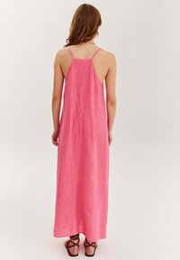 Ružová maxi šaty z ľanu s tenkými ramienkami, voľným strihom a nízkym pásom. Textúrovaná látka splýva až do dĺžky členkov a je doplnená sandálmi na remienky.