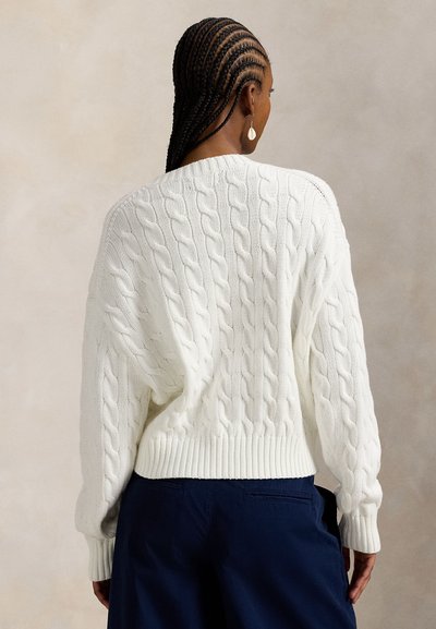 Χοντρό λευκό πουλόβερ με πλέξη κόμπου, με χαμένες ραφές στους ώμους, ριμπ στα τελειώματα και στα μανίκια, συνδυασμένο με σκούρο παντελόνι. Η πίσω όψη δείχνει την υφή του μοτίβου.