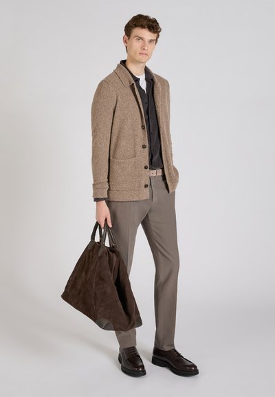 Jasnobrązowy kardigan o teksturowanym wykończeniu, czarna koszula pod spodem, beżowe spodnie i ciemnobrązowa torebka z zamszu z skórzanymi akcentami.