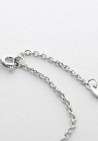 Silver kedja halsband med fokus på låset och de överlappande ovala länkarna mot en enkel ljus bakgrund.