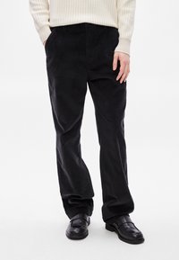 Μαύρο παντελόνι από κορντόρας με ίσια γραμμή, διαθέτει πλαϊνές τσέπες και υφή, συνδυασμένο με μαύρα loafers.