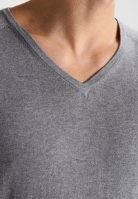 Pull gris à col en V en tissu tricoté, présentant une texture lisse et un léger éclat. L'encolure est renforcée par une couture discrète.
