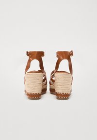 Bruine leren sandaaltjes met straps en een gevlochten jute hak. De hak heeft een textuur, met witte stiksels langs de basis.