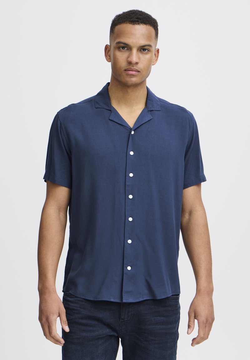 Camicia a maniche corte blu navy con colletto in un tessuto leggero, caratterizzata da una chiusura con bottoni e una leggera lucentezza. Tessuto morbido con vestibilità rilassata.