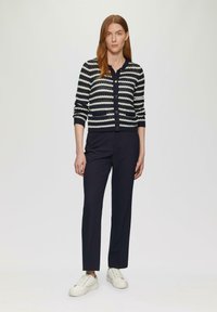 Cardigan a strisce navy e bianche in maglia con collo rotondo, chiusura con bottoni e due tasche frontali; abbinato a pantaloni scuri e sneakers bianche.