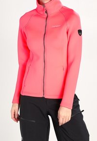 Veste ajustée à manches longues de couleur rose vif, avec un col haut et une fermeture éclair complète. Présente un logo sur l'épaule gauche et deux poches zippées.