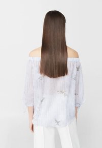 Off-Shoulder-Oberteil aus leichtem, gestreiftem Stoff mit zarter floralem Stickerei. Lockere Passform mit Dreiviertelärmeln und weicher Textur.