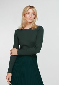 Ciemnozielony prążkowany top z okrągłym dekoltem, zestawiony z plisowaną ciemnozieloną spódnicą. Gładka tekstura i długie rękawy dopełniają całość.