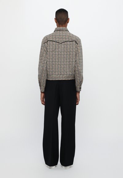 Collared cropped jacket in multicolored tweed with a check pattern, featuring black trim. Paired with wide-leg black pants and white shoes.