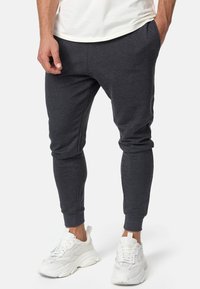 Dunkelgraue Jogginghosen aus weichem Stoff, mit einem tapered Bein Design und elastischen Bündchen, kombiniert mit weißen Sneakern.