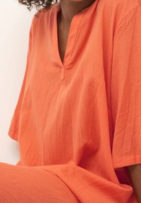 Orange linnekjortel med V-ringning och korta ärmar, med en avslappnad passform och subtil textur.