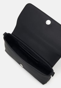 Bolso bandolera de cuero negro con acabado liso, compartimento abierto y cierre a presión plateado. El interior cuenta con una ranura para tarjetas.