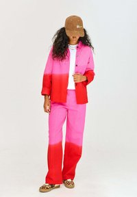 Kurtka w gradiencie przechodzącym od czerwonego do różowego, w zestawieniu z dopasowanymi różowymi spodniami. Uzupełniona brązową czapką i wzorzystymi butami.