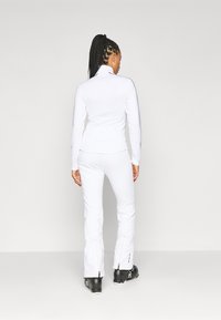 Set format din bluză albă cu mânecă lungă și pantaloni asortați, cu un design fără cusături, fabricat dintr-un material ușor, cu accente negre pe mâneci și fermoare la tivurile pantalonilor.