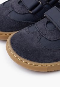 Scarpe in suede e pelle blu navy con un cinturino in Velcro, dotate di suola in gomma e dettagli testurizzati per una maggiore aderenza. Forma arrotondata con cuciture decorative.