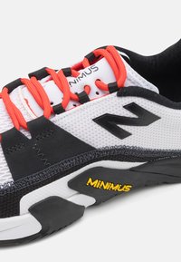 Hvide mesh atletik sko med sorte accenter, røde snørebånd og "MINIMUS" logo. Har en tekstureret sål til trækkraft og støtte.