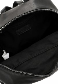 Czarna skórzana torba na plecy od środka z zamykaną kieszonką i gładką teksturą. Zawiera białą tubę. Minimalistyczny design i monochromatyczna kolorystyka.