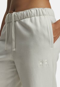 Pantalons de jogging gris clair avec une taille élastique froncée, cordon de serrage ajustable, poches latérales et logo Under Armour en relief sur la cuisse.