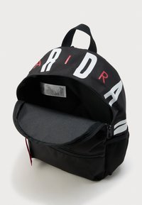 Μαύρο σακίδιο με μερικώς ανοιχτό βασικό διαμέρισμα, κόκκινα και λευκά γράμματα «Adidas» στο πάνω μέρος, μπροστινή τσέπη με φερμουάρ και πλέγμα πλευρική τσέπη.