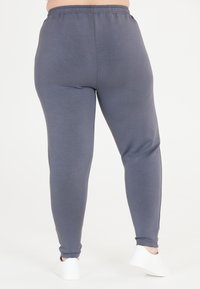 Grå, stretchiga leggings med ett elastiskt midjeband. Materialet är slätt med en sleek textur och smalnar av till ankellängd. Matchas med vita skor.