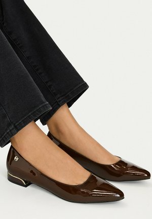 Ballerine in vernice marrone con punta appuntita indossate con pantaloni neri su sfondo chiaro.