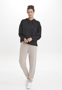 Svart hooded sweatshirt med dragsnören, avslappnad passform, kombinerad med ljusbeiga tapered-byxor, bärs med vita sneakers, slät tygtextur.