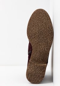 Zamszowy but w kolorze bordowym z teksturowaną brązową gumową podeszwą, wyposażony w boczny zamek błyskawiczny i gładką powierzchnię wierzchnią.