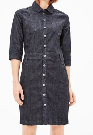 Mørk denim-knap-op kjole med trekvartærmer, brystlommer og en figursyet talje båret af en stående person.