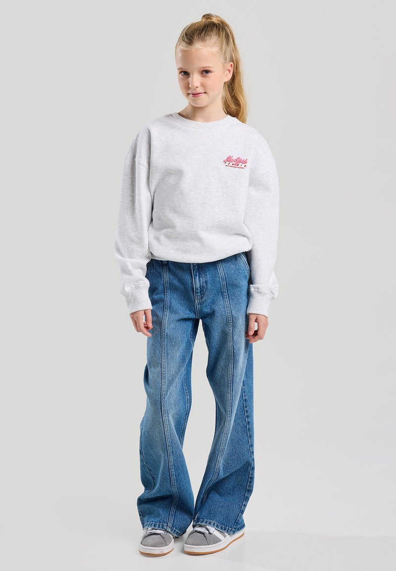 Grey sweatshirt with a small pink graphic on the chest, paired with light blue wide-leg jeans. The jeans have visible seams.