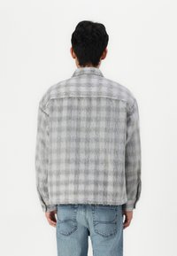 Grijze geruite jas van zacht, textuurstof. Bevat een kraag met knopen, een borstzak en een losse pasvorm, gecombineerd met lichtblauwe denim.