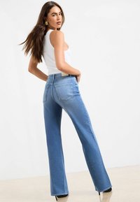 Gai zils augstās jostas flared džinsi ar piecām kabatām, gludu tekstūru un tīru apdari; saskaņoti ar pieguļošu baltu topu bez piedurknēm.