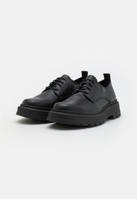 Scarpe stringate in pelle nera con suola in gomma spessa e dettagli testurizzati. Caratterizzate da una punta arrotondata e un anello per un facile indossamento.