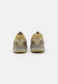 Två par gula träningsskor med grå akcenter och en texturerad yta, med en flik på baksidan och synlig varumärkeslogotyp.