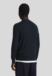 Marinblå tröja med rund halsringning, långa ärmar och ribbade muddar. Materialet verkar slätt med en klassisk passform och subtil textur.