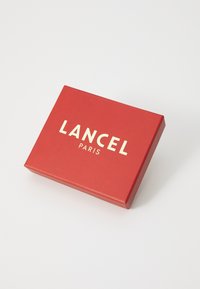Rød rektangulær boks med en jevn tekstur, med "LANCEL PARIS" i fete gullbokstaver på toppen.