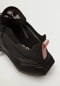 Black sneaker with mesh and textured upper, pink accents, visible logo on the insole, and a thick, curved black sole.