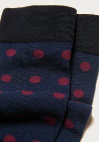 Dunkelblaue Socken mit schwarzen Bündchen und kastanienbraunen Punkten, die in einem verstreuten Muster angeordnet sind.