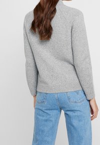 Grå stickad tröja med ribbad nederkant och långa ärmar, i kombination med ljusblå denimjeans, som visar en avslappnad passform och mjuk textur.