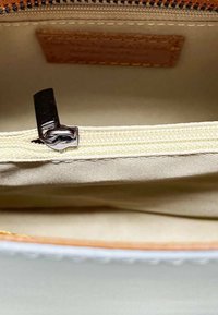 Bolsa con cremallera de interior beige, cremallera de metal plateado y ribete de lona beige cosido. Cuenta con una etiqueta de cuero en el interior.