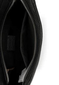 Interno di borsa in pelle nera con chiusura a zip, caratterizzato da pelle testurizzata, un compartimento centrale e una piccola etichetta.