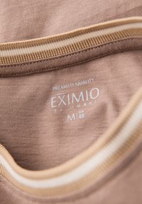 Brauner Baumwoll-T-Shirt-Kragen mit beigen gestreiften Akzenten und einem Etikett, das "EXIMIO" und die Größe M (EUR 48) anzeigt. Der Text ist in Weiß.