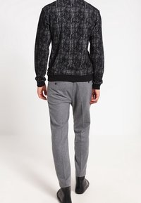 Czarny sweter o fakturze, z jednolitym paskiem w talii, w połączeniu z jasno szarymi, dopasowanymi spodniami. Stylizację uzupełniają czarne botki za kostkę.