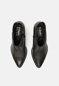 Bottines en cuir noir avec un bout pointu, comportant une fermeture éclair sur le côté, des coutures courbées et une semelle intérieure à motifs. Texture lisse dans l'ensemble.